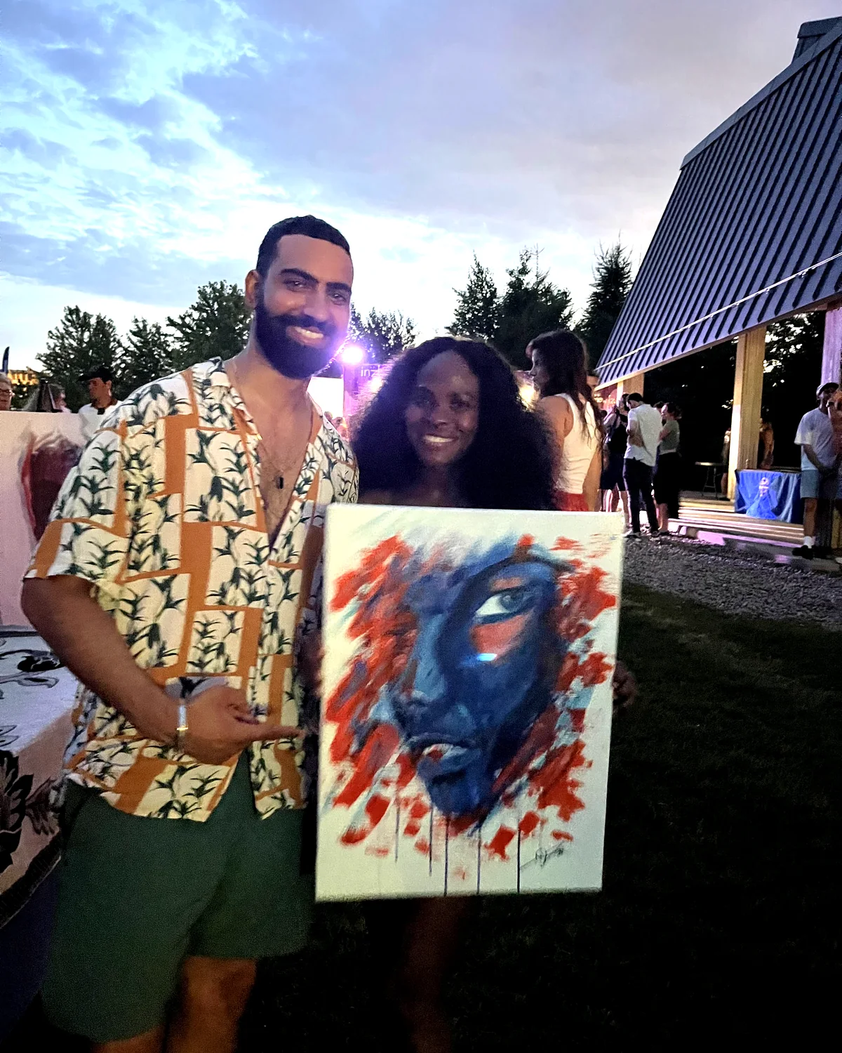 A collector holding her portrait beside Amit at one of his live painting events