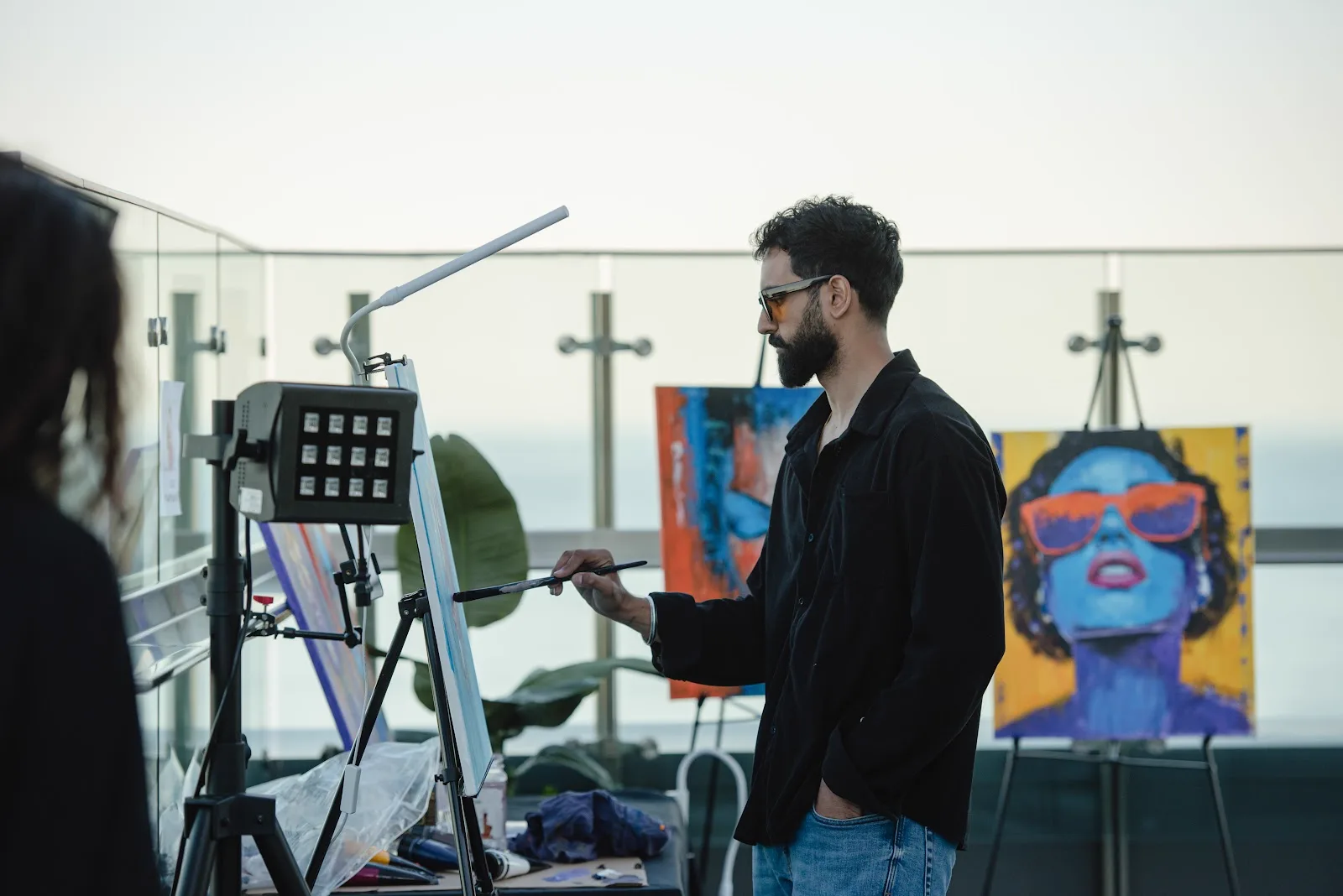 Amit Tejpal painting live at a rooftop event, finished portraits on easels beside him